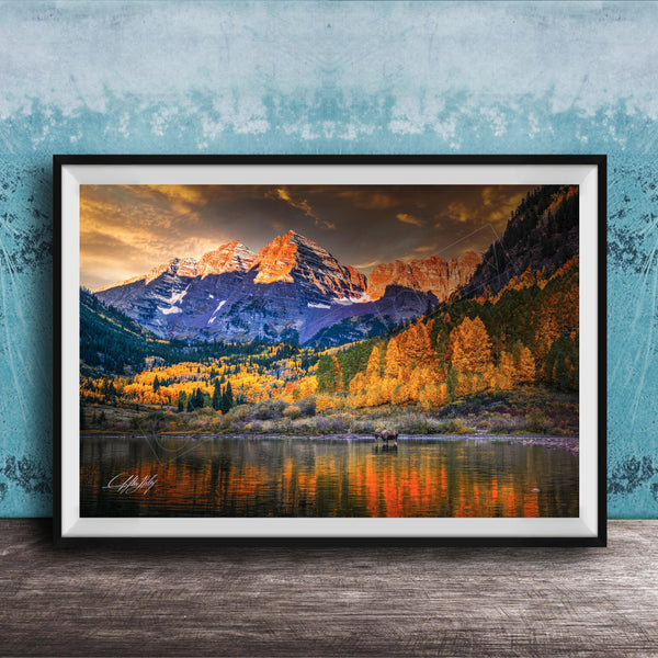The image is a framed photograph depicting a scenic mountain landscape with a lake in the foreground, surrounded by trees with autumn foliage.