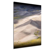 a vast, expansive landscape with towering sand dunes stretching across the horizon. The dunes are covered in a light beige color, contrasting with the darker blue of the sky above. The terrain is dotted with patches of green vegetation, adding a touch of life to the otherwise barren landscape. The image is a striking visual representation of the natural beauty of the desert environment.