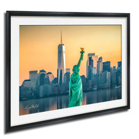 a framed photograph of the Statue of Liberty in the foreground, with the New York City skyline in the background.