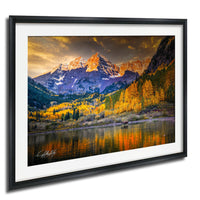 a breathtaking mountain landscape with a lake in the foreground, surrounded by vibrant fall foliage. The mountains are covered in snow, and the sky is filled with clouds, creating a dramatic backdrop. The colors in the image are predominantly orange, yellow, and green, reflecting the autumn season. The overall scene is a stunning representation of nature's beauty and the changing seasons.