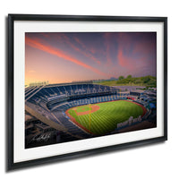 A framed photograph of a baseball stadium at sunset, with the field and seating areas visible.