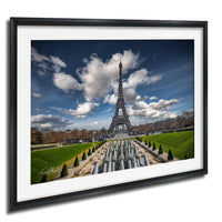 the Eiffel Tower in Paris, France, with a cloudy blue sky and lush green gardens in the foreground.