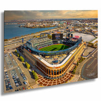 An aerial view of a large baseball stadium with a large field, surrounded by a cityscape and a body of water.