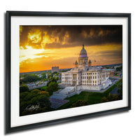 A framed photograph of a large, ornate building with a domed roof, set against a dramatic sky with orange and yellow hues, likely at sunset.