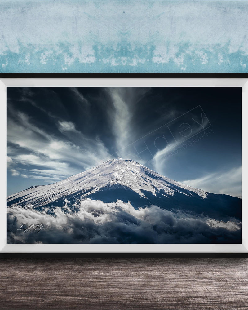 A framed photograph of a snow-capped mountain peak, with dramatic clouds and a dramatic sky in the background.