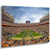 A crowded football stadium with a large audience, featuring a football field, cheerleaders, and a large scoreboard.