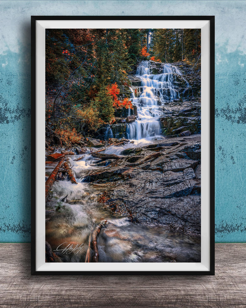 A framed photograph of a waterfall cascading down a rocky cliff surrounded by vibrant autumn foliage.
