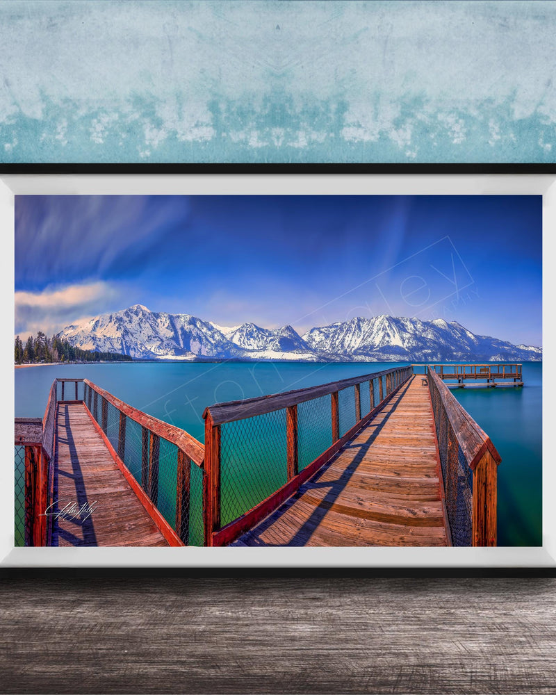 A framed photograph of a wooden pier extending into a serene lake, with snow-capped mountains in the background.