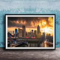 A framed photograph of a city skyline at sunset, with the sun setting behind the buildings and casting a warm, golden glow over the scene.