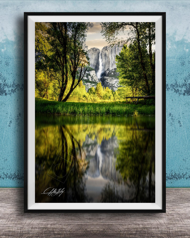 A framed photograph of a serene landscape with a waterfall reflected in a calm lake, surrounded by lush greenery and trees.