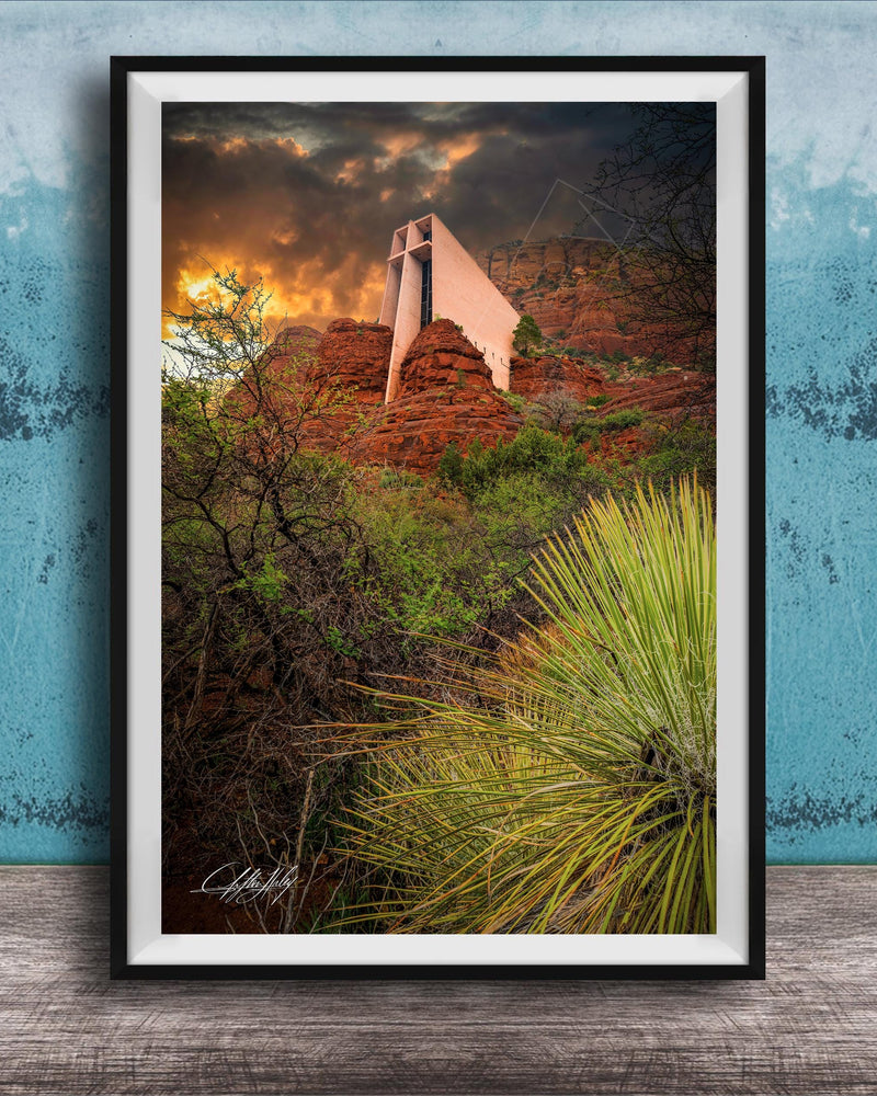 a framed photograph of a desert landscape with a large, white structure in the background, possibly a building or monument, set against a dramatic sky with clouds and a sunset.