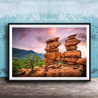 A framed photograph of a striking rock formation with two large, stacked rock pillars set against a vibrant sunset sky.