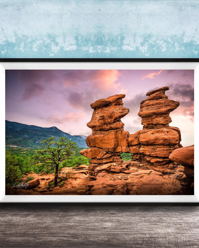 A framed photograph of a striking rock formation with two large, stacked rock pillars set against a vibrant sunset sky.