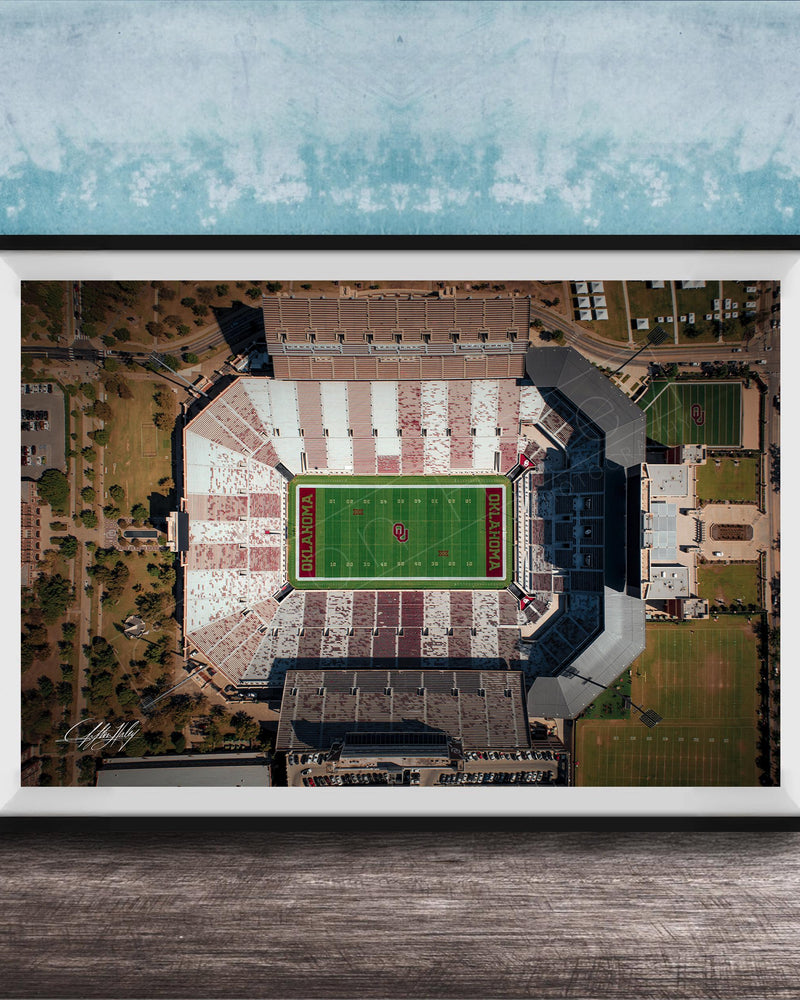 The image is an aerial view of a football stadium with a green field and surrounding buildings.