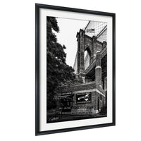 A black and white photograph of the Brooklyn Bridge, with the American flag flying atop the structure.
