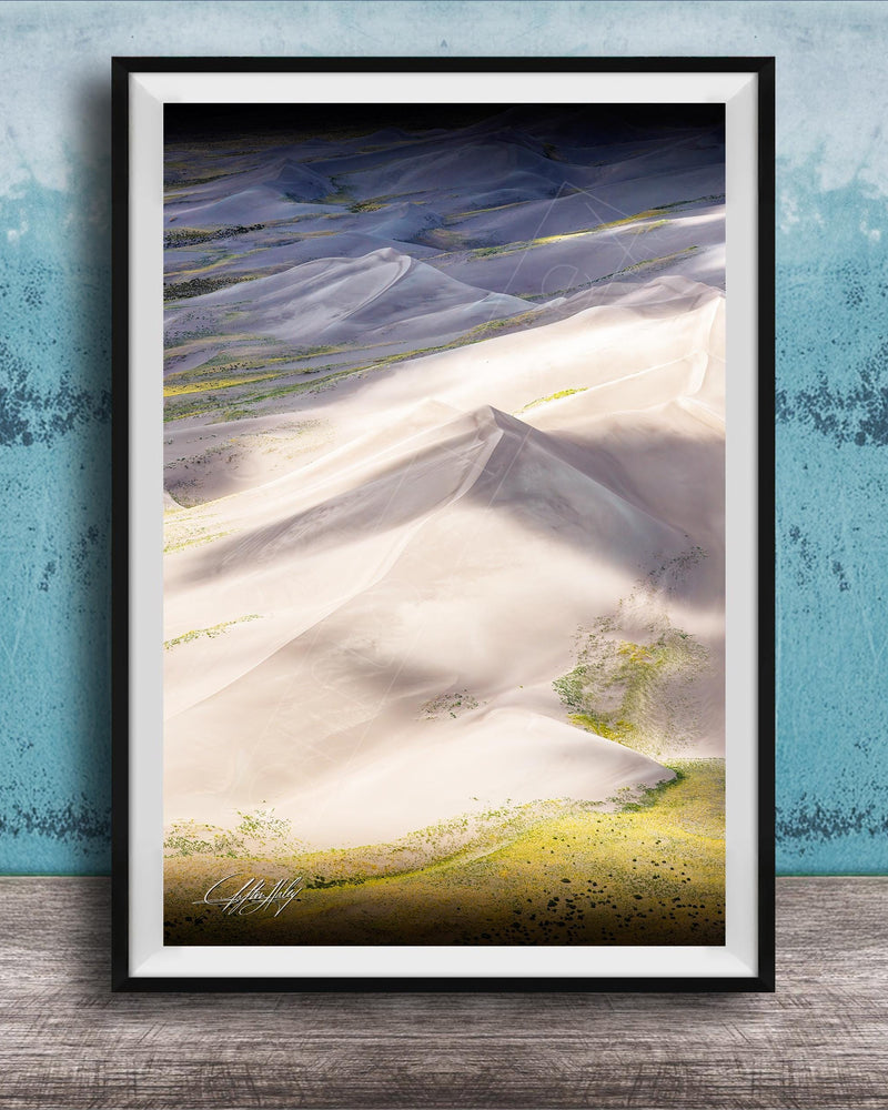 The image is a framed photograph of a mountainous landscape with white sand dunes and patches of green vegetation.