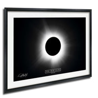 The image is a framed photograph depicting a total solar eclipse, with the moon completely obscuring the sun and creating a bright, white ring around it.