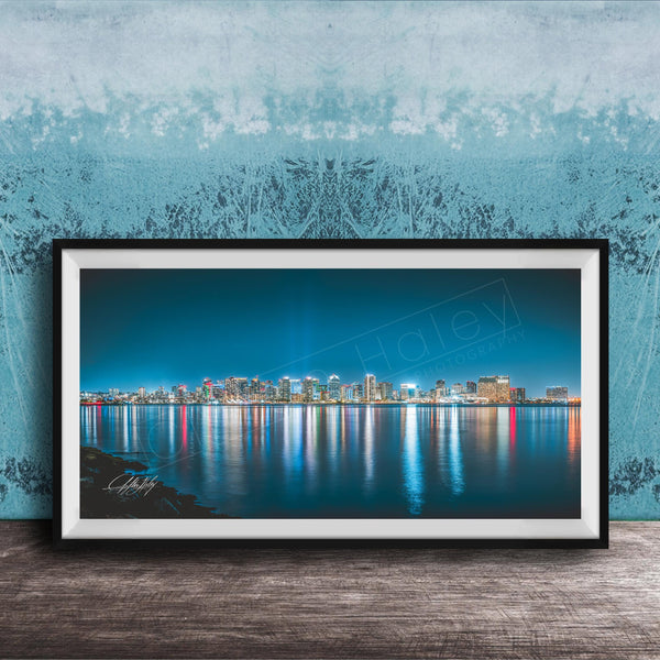 A framed photograph of a city skyline at night, with the buildings' lights reflected in the water below.