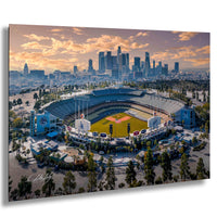 An aerial view of a baseball stadium with the city skyline in the background, set against a colorful sunset sky.