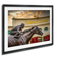 A bronze statue of a jockey riding a horse in front of a building with the sign "Churchill Downs" displayed.