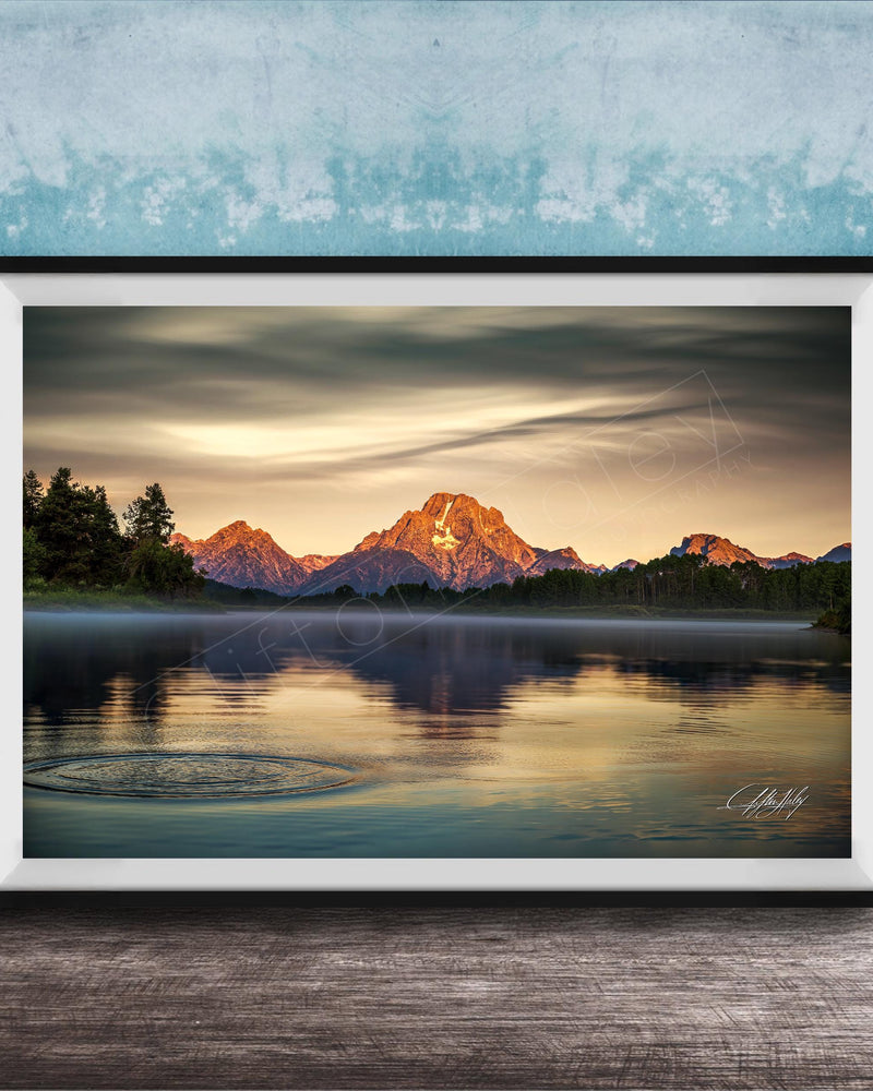 A framed photograph depicting a serene mountain landscape at sunset, with a calm lake reflecting the warm colors of the sky.
