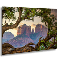 a breathtaking view of a mountainous landscape, with towering red rock formations silhouetted against a vibrant sky. The photograph is framed by a twisted tree branch, adding a touch of nature's artistry to the scene. The image is a captivating blend of natural beauty and artistic composition, showcasing the grandeur of the landscape and the intricate details of the rock formations.