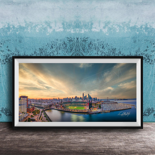 The image is a framed photograph of a cityscape at sunset, featuring a skyline with tall buildings and a body of water in the foreground.