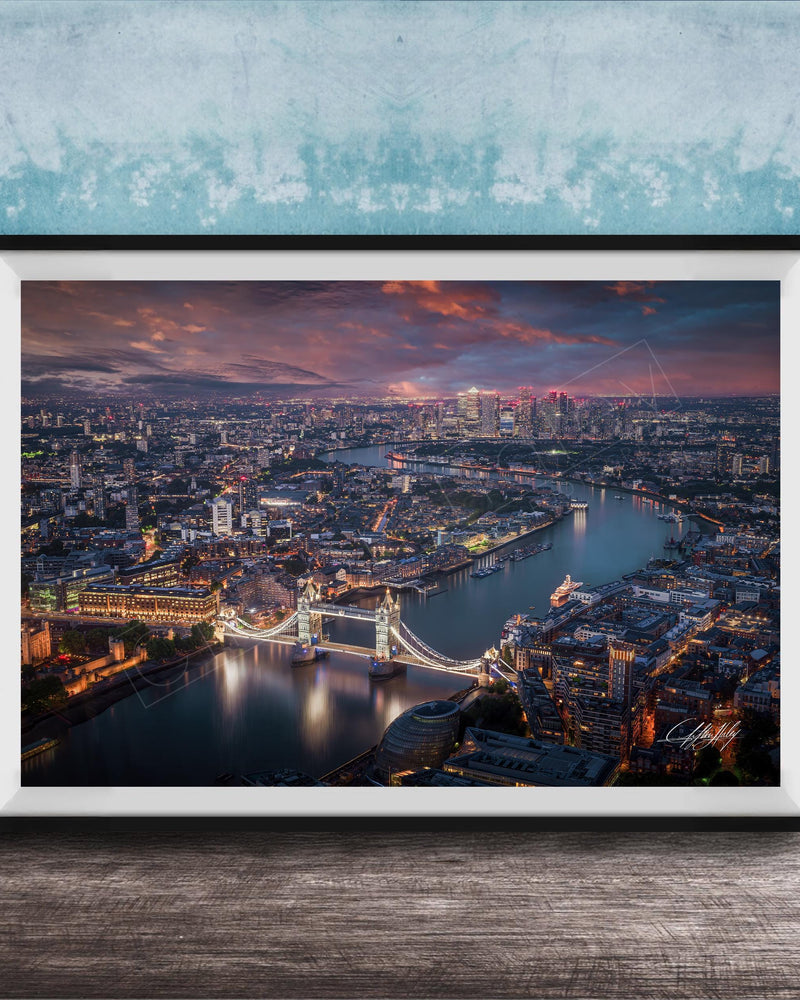 The image is a framed aerial view of a city at night, showcasing a bridge and the city skyline with illuminated buildings and a river.