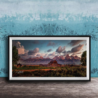 A framed photograph depicting a serene rural landscape with a barn, mountains, and a blue sky with clouds at sunset.