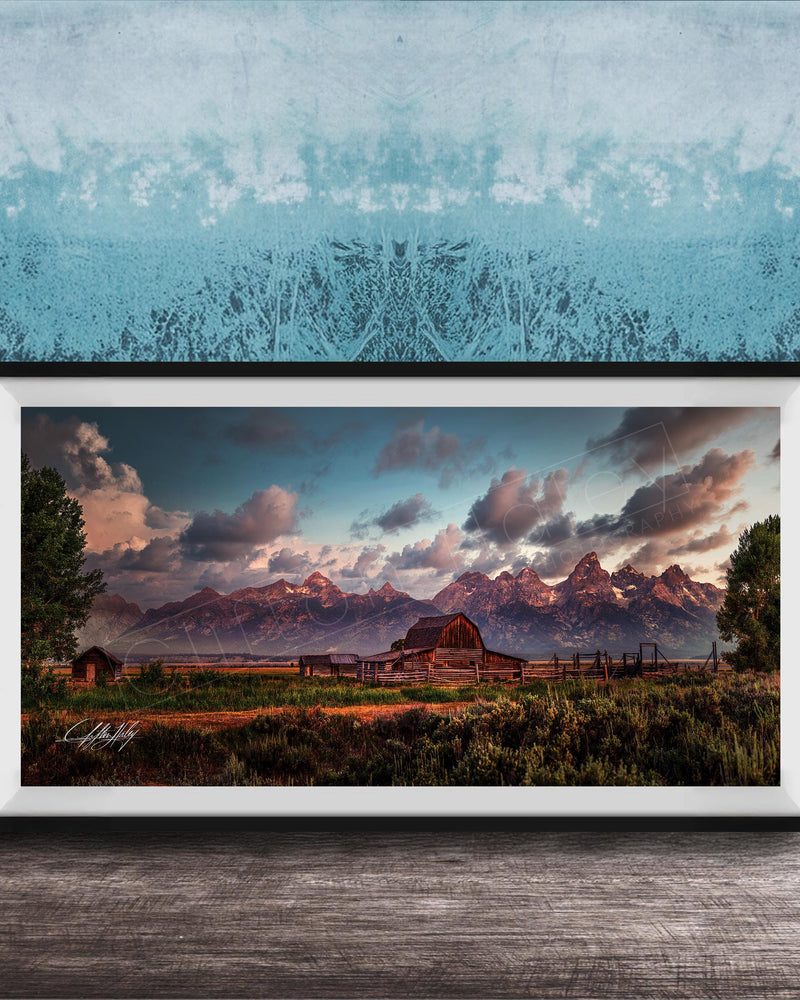 A framed photograph depicting a serene rural landscape with a barn, mountains, and a blue sky with clouds at sunset.
