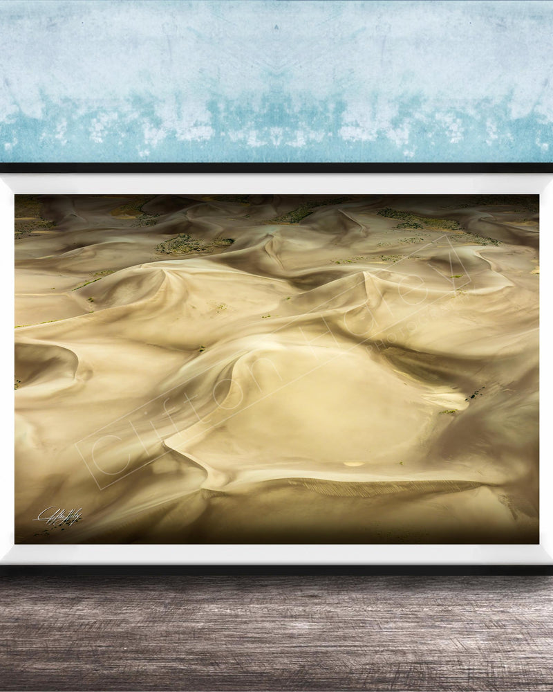 The image is a framed photograph of sand dunes, with a blue wall in the background.