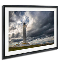 A white lighthouse with a black top stands tall against a dramatic sky filled with dark clouds.