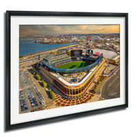 The image is an aerial view of a baseball stadium with a large field, surrounded by a cityscape.
