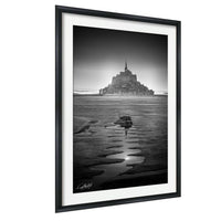 A black and white photograph of a castle or fortification situated on a beach, with the water receding in the foreground and the sky above.