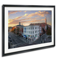 a city street scene with buildings, traffic lights, and a clock tower in the background, set against a colorful sunset sky.