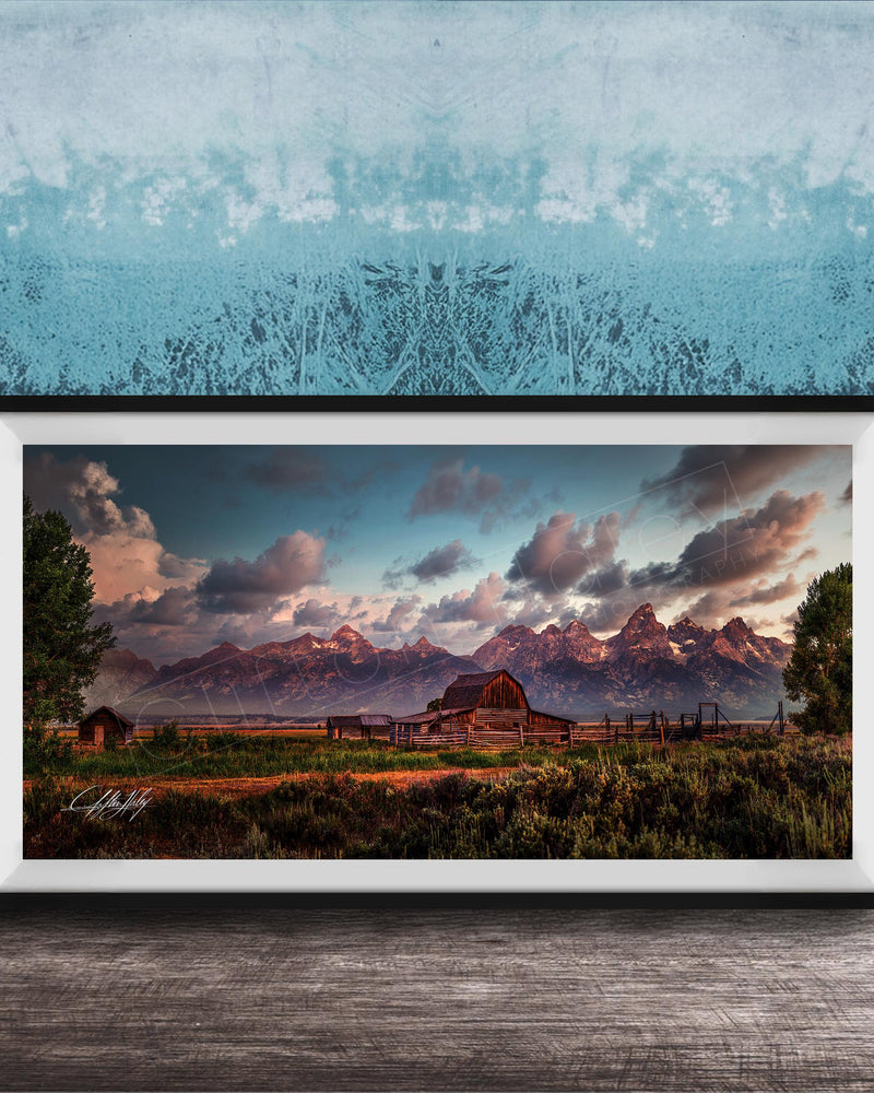 A framed photograph depicting a serene rural landscape with a barn, mountains, and a blue sky with clouds at sunset.