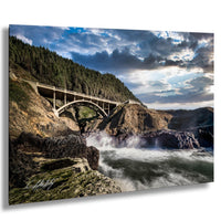 a concrete bridge spanning over a rocky, mountainous landscape with crashing waves in the foreground.