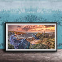 The image is a framed photograph of a scenic coastal landscape with rugged cliffs, a rocky shoreline, and a dramatic sunset over the ocean.