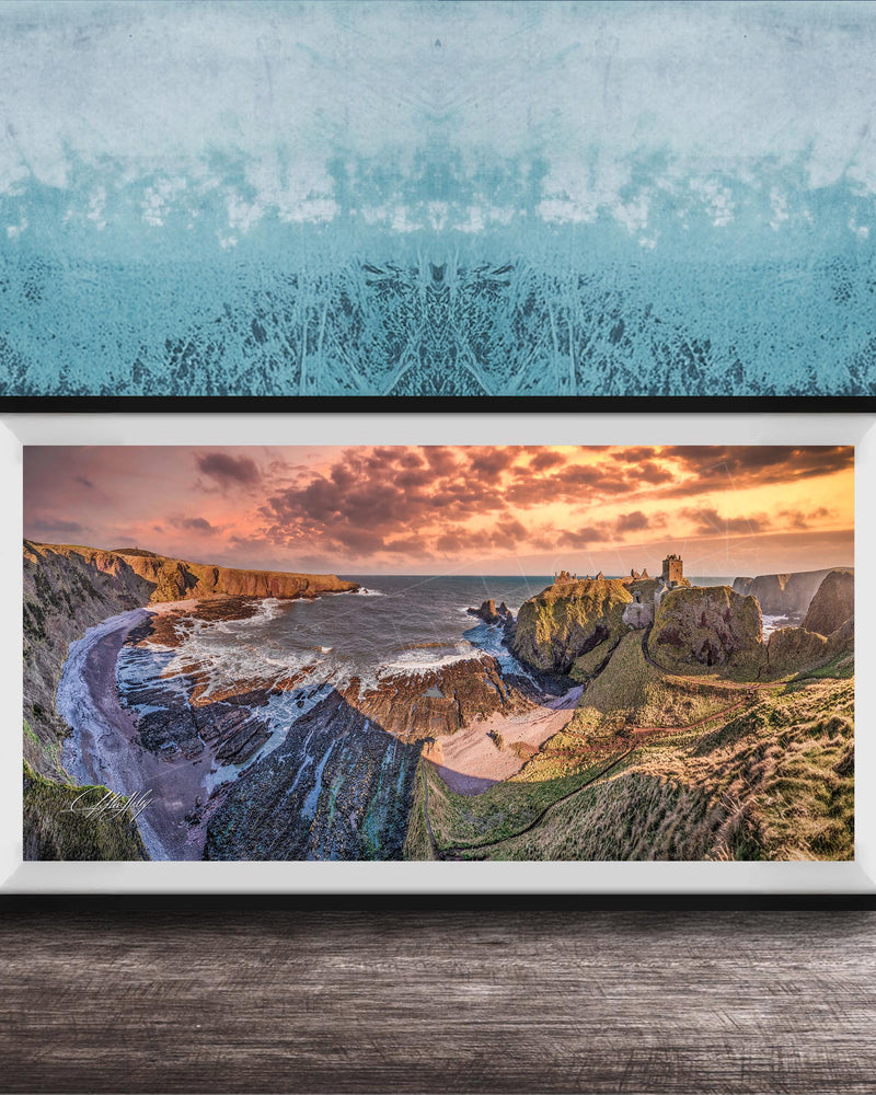 The image is a framed photograph of a scenic coastal landscape with rugged cliffs, a rocky shoreline, and a dramatic sunset over the ocean.
