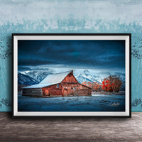 A rustic wooden barn stands in a snowy landscape, with a mountain range in the background under a dark, cloudy sky.