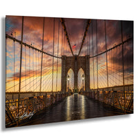 a suspension bridge with a wooden deck and metal railing, set against a dramatic sky with colorful clouds and a setting sun.