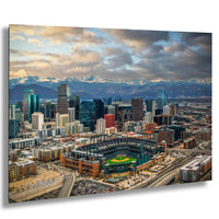 a large city with a baseball stadium in the center, surrounded by tall buildings and mountains in the background.
