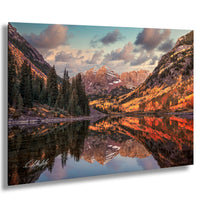 a serene mountain landscape with a lake reflecting the vibrant colors of the autumn foliage. The mountains are adorned with a mix of green and brown, creating a beautiful contrast against the clear blue sky. The lake is surrounded by trees with orange and yellow leaves, adding a warm and cozy atmosphere to the scene. The image is a captivating representation of nature's beauty and the tranquility of the mountains.