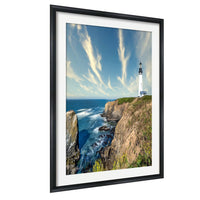 A framed photograph depicting a lighthouse on a cliff overlooking the ocean, with a cloudy blue sky in the background.