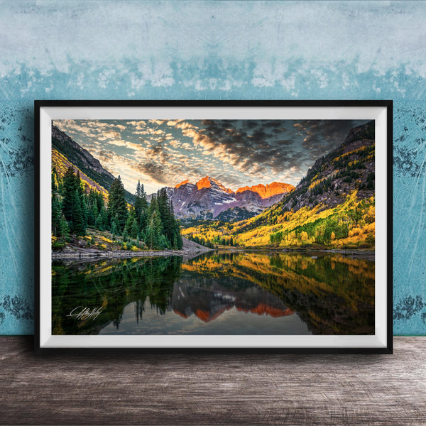 The image is a framed photograph depicting a serene mountain landscape with a lake reflecting the vibrant colors of the sky and surrounding trees.