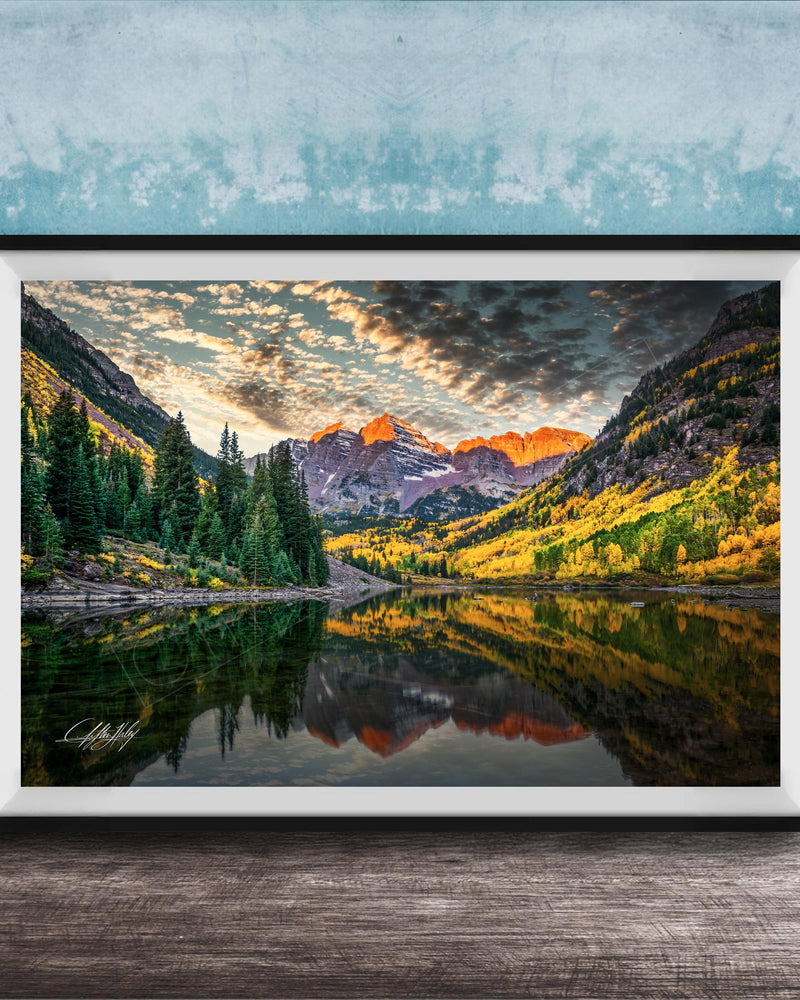 The image is a framed photograph depicting a serene mountain landscape with a lake reflecting the vibrant colors of the sky and surrounding trees.