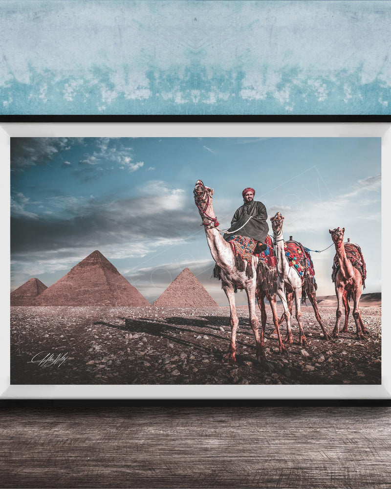 A framed photograph depicting a camel caravan in front of the iconic pyramids of Giza in Egypt.