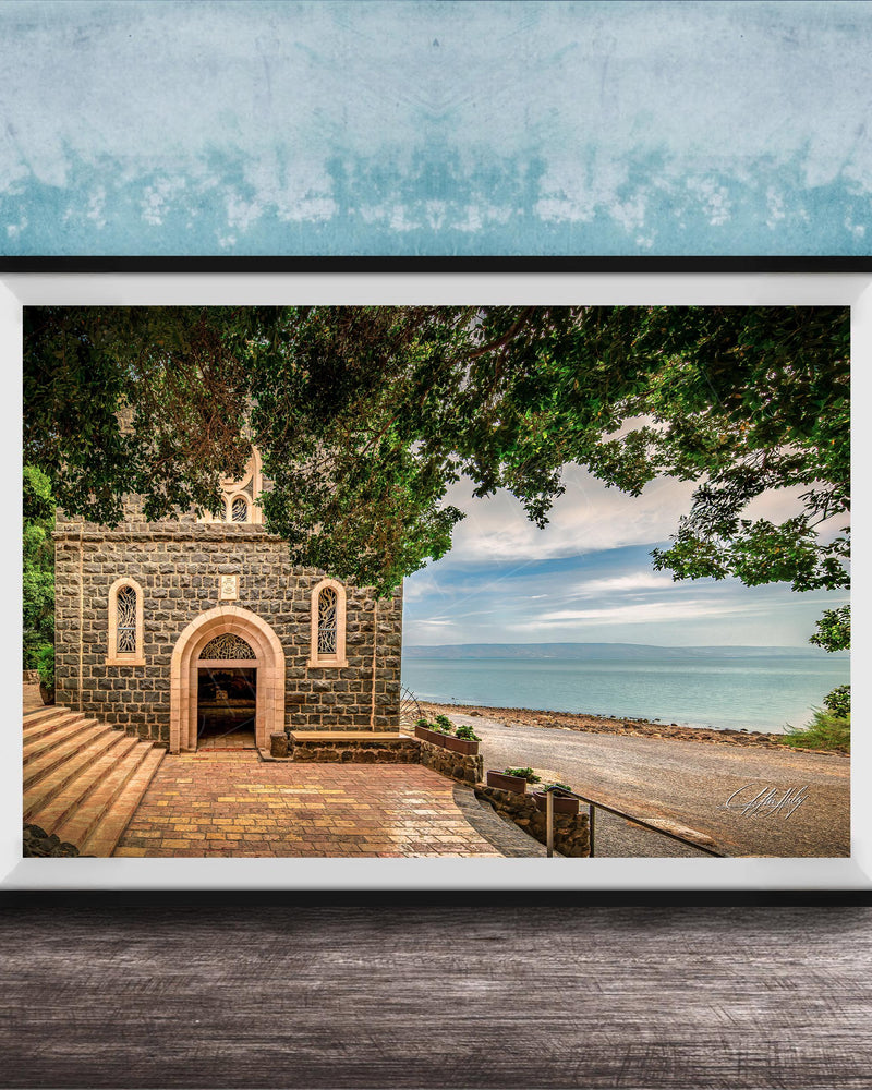 A framed photograph depicting a stone building with arched windows and a stone walkway leading to a beach with a blue sky and trees in the background.