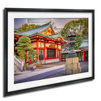 A framed photograph depicting a traditional Japanese temple with a red roof and green walls, surrounded by trees and a stone fountain.