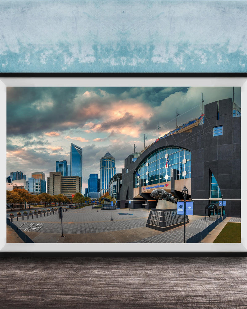 A framed photograph of a cityscape with tall buildings, a large arch structure, and a cloudy sky in the background.